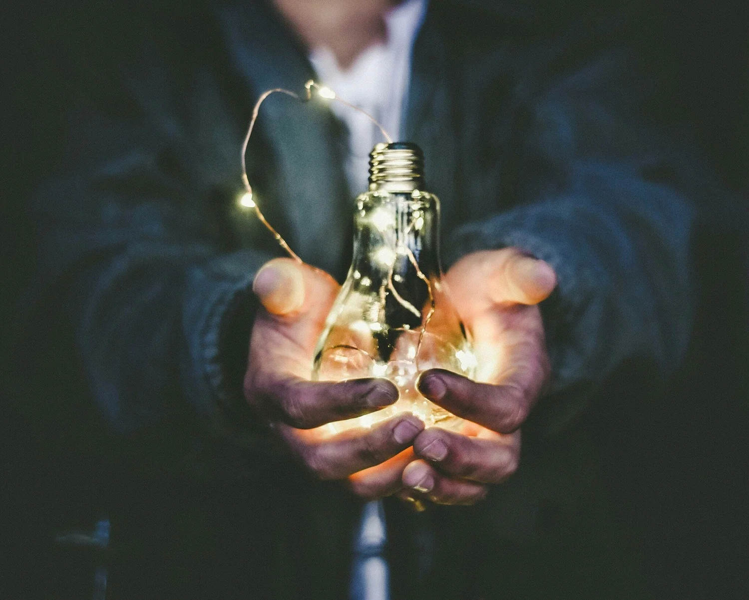 A person holding an illuminated light bulb