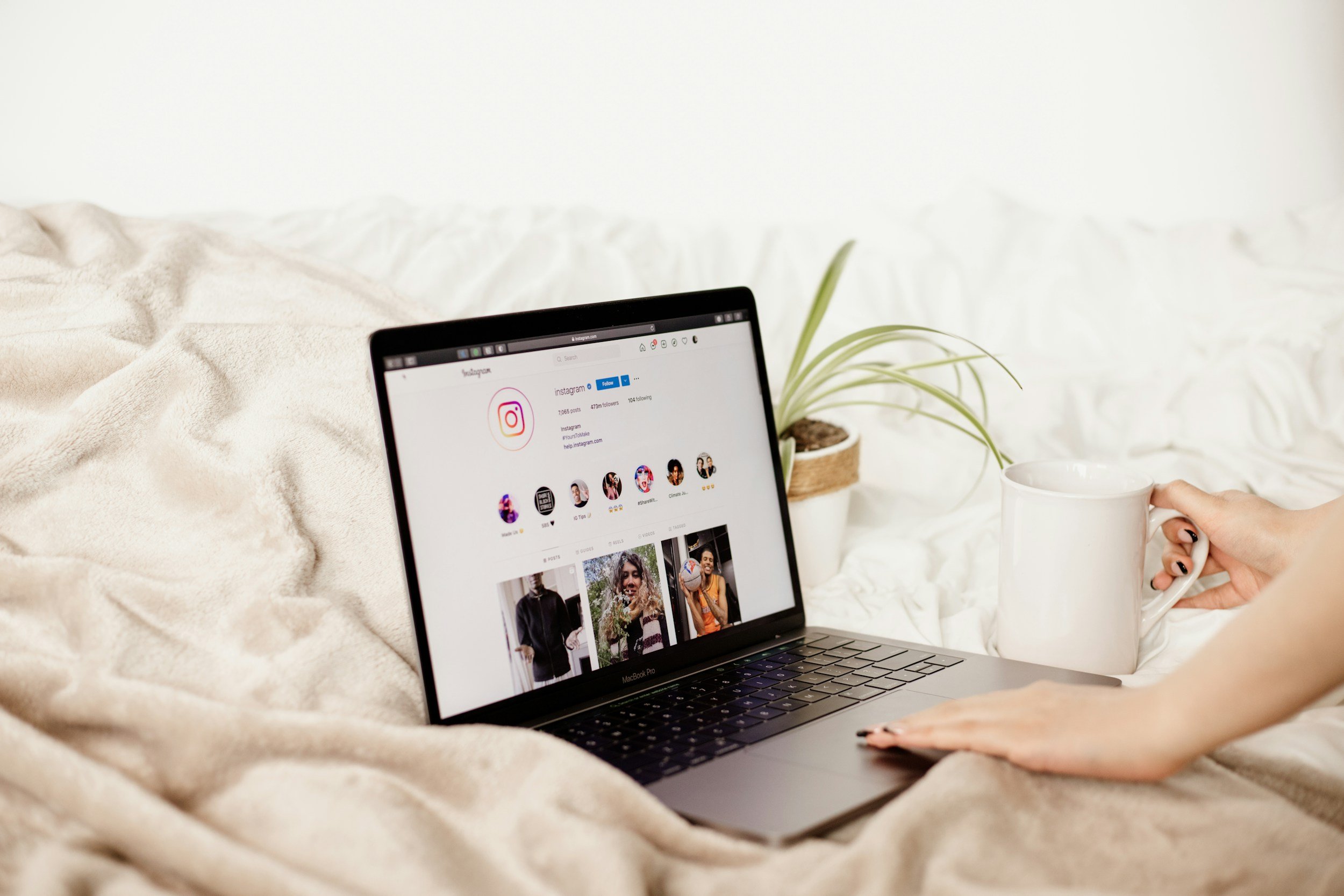 Instagram displayed on a laptop beside a plant and coffee cup